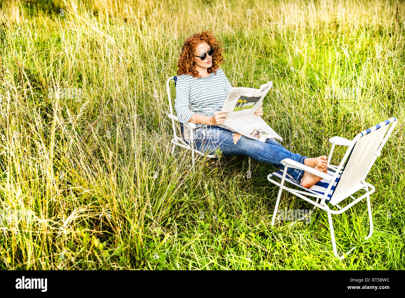 Mujer joven relajándose en una pradera la lectura de periódicos Foto de stock