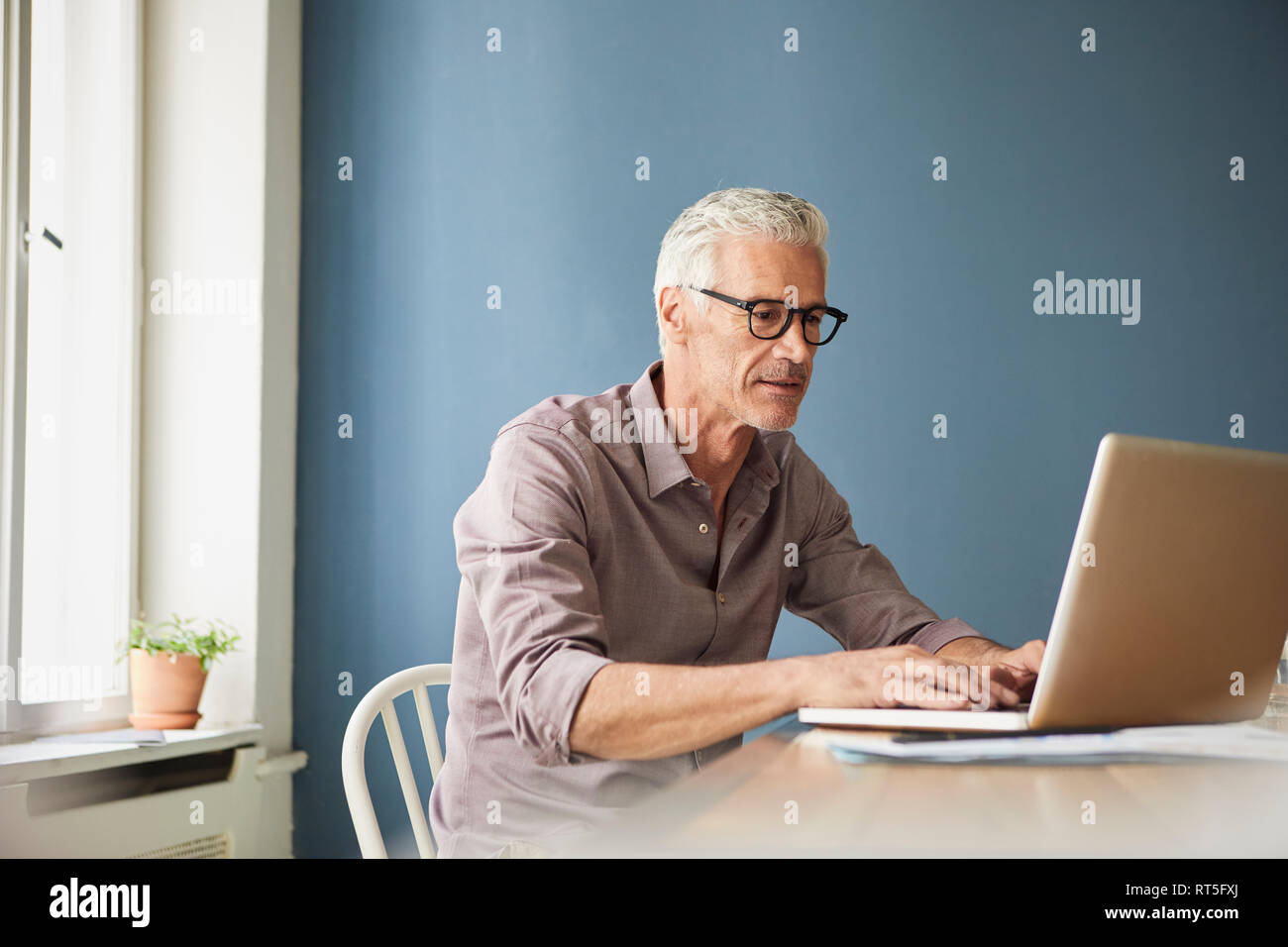 Hombre maduro con ordenador portátil sobre la mesa en casa Foto de stock