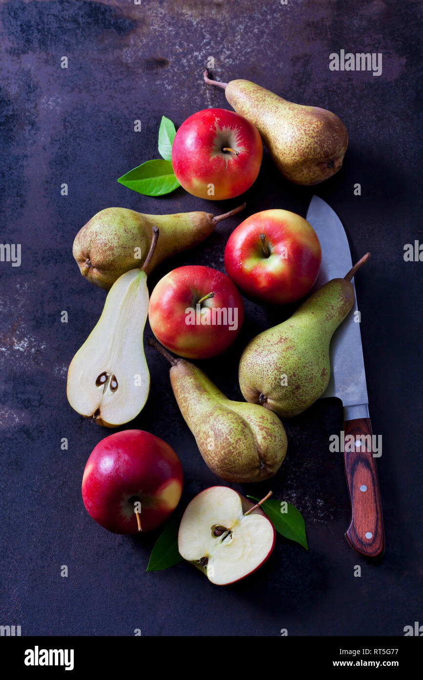En rodajas finas y las manzanas y las peras enteras en tierra oscura Foto de stock