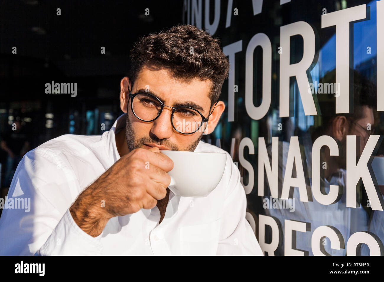 Retrato de joven empresario de beber café en el café en la acera observando algo Foto de stock