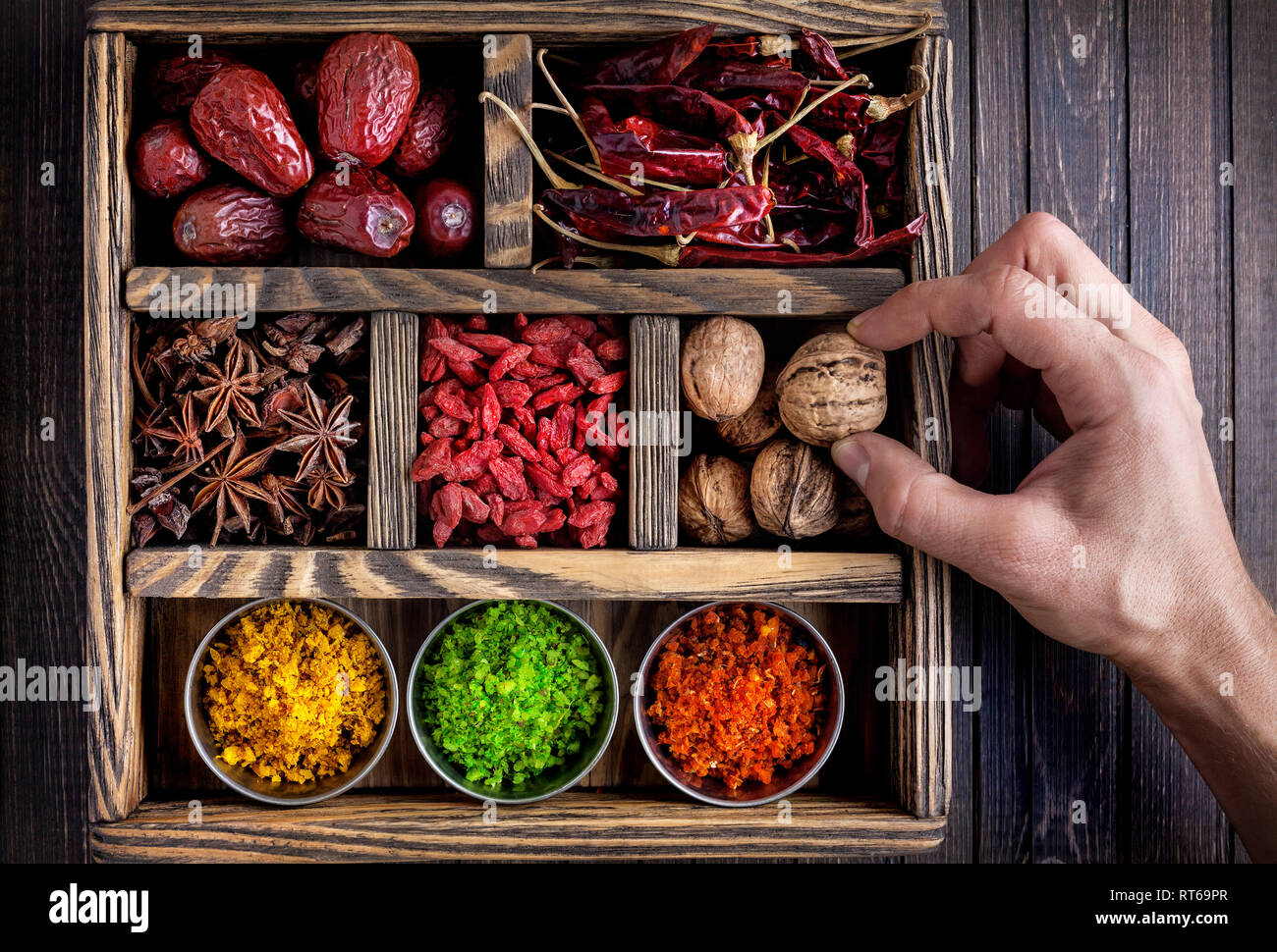 Las especias, los frutos secos y la mano que sostiene la nuez en la caja de madera Foto de stock