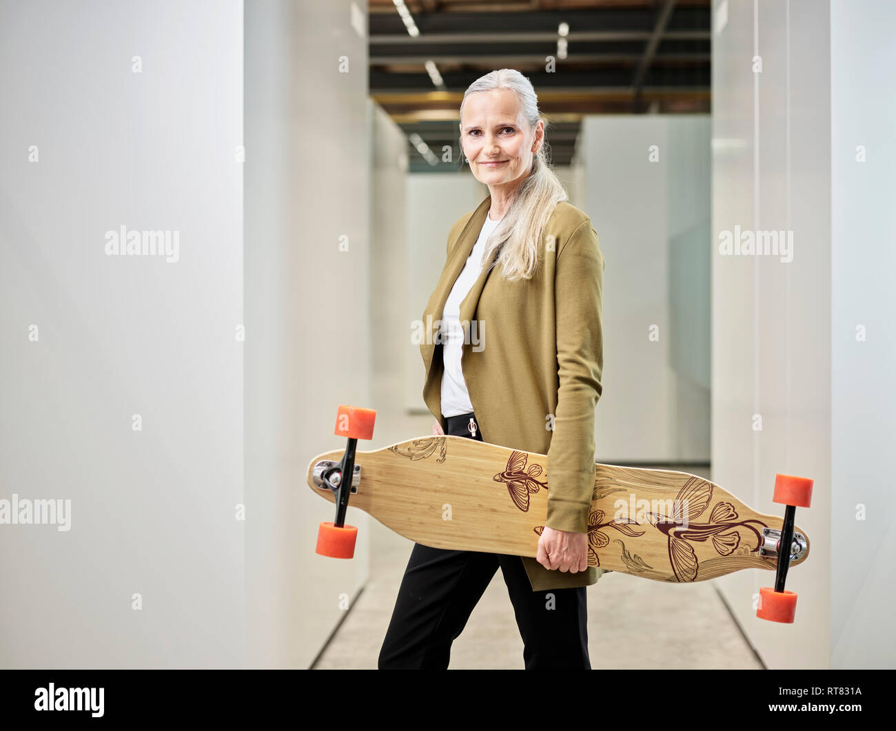 Retrato de la empresaria llevando longboard sobre el suelo de su oficina Foto de stock