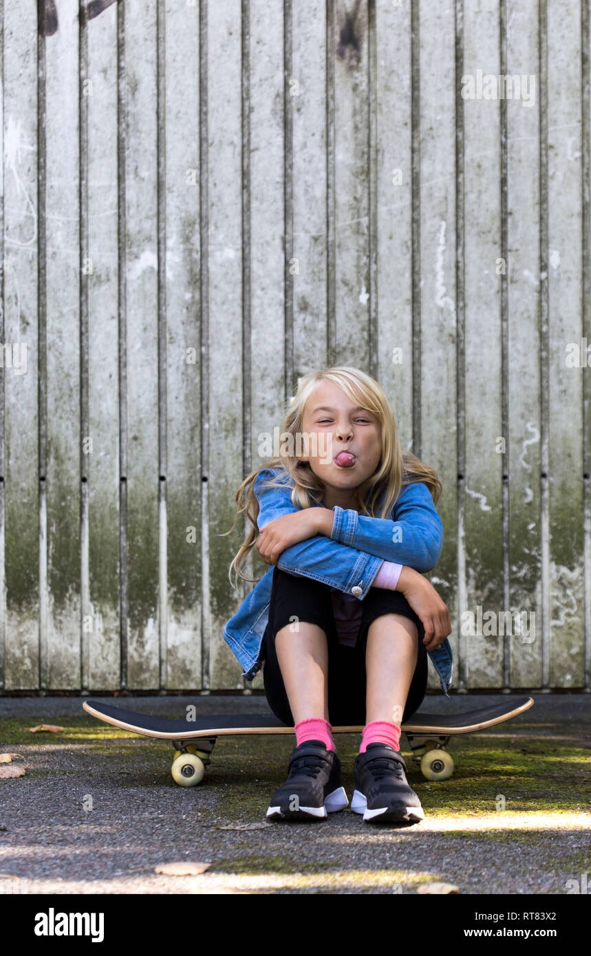 Retrato de chica sentada en monopatín en frente de pared de madera fuera la lengua Foto de stock