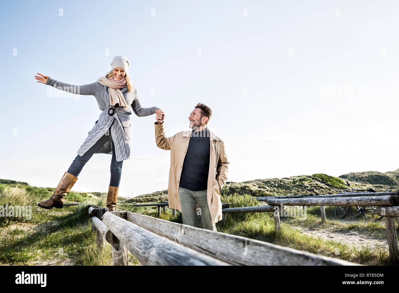 Hombre ayudando a mujer equilibrio sobre estacas de madera en las dunas Foto de stock