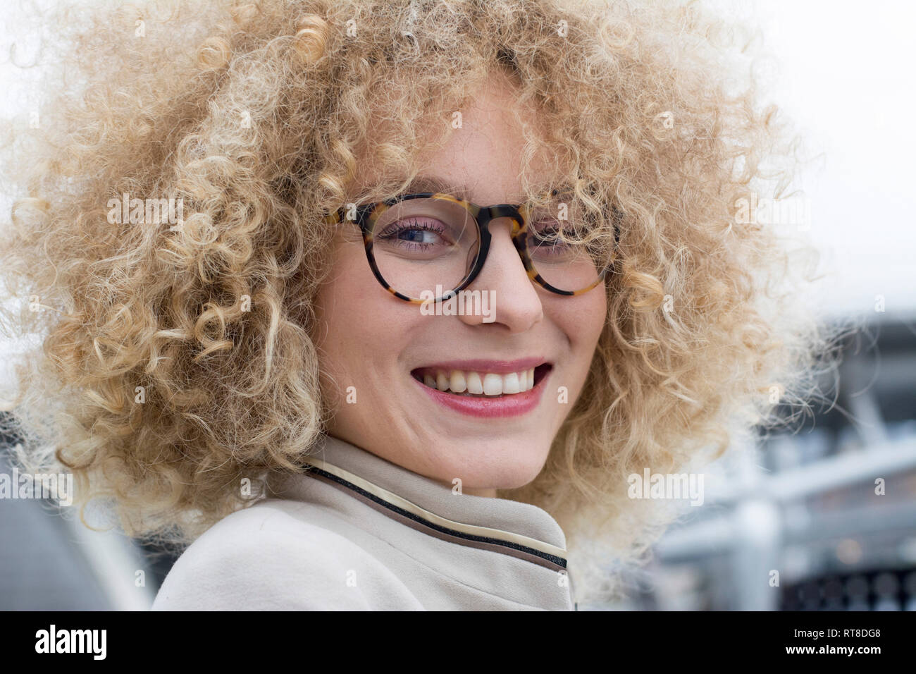 Retrato de mujer rubia sonriendo con tirabuzones llevaba gafas de moda Foto de stock
