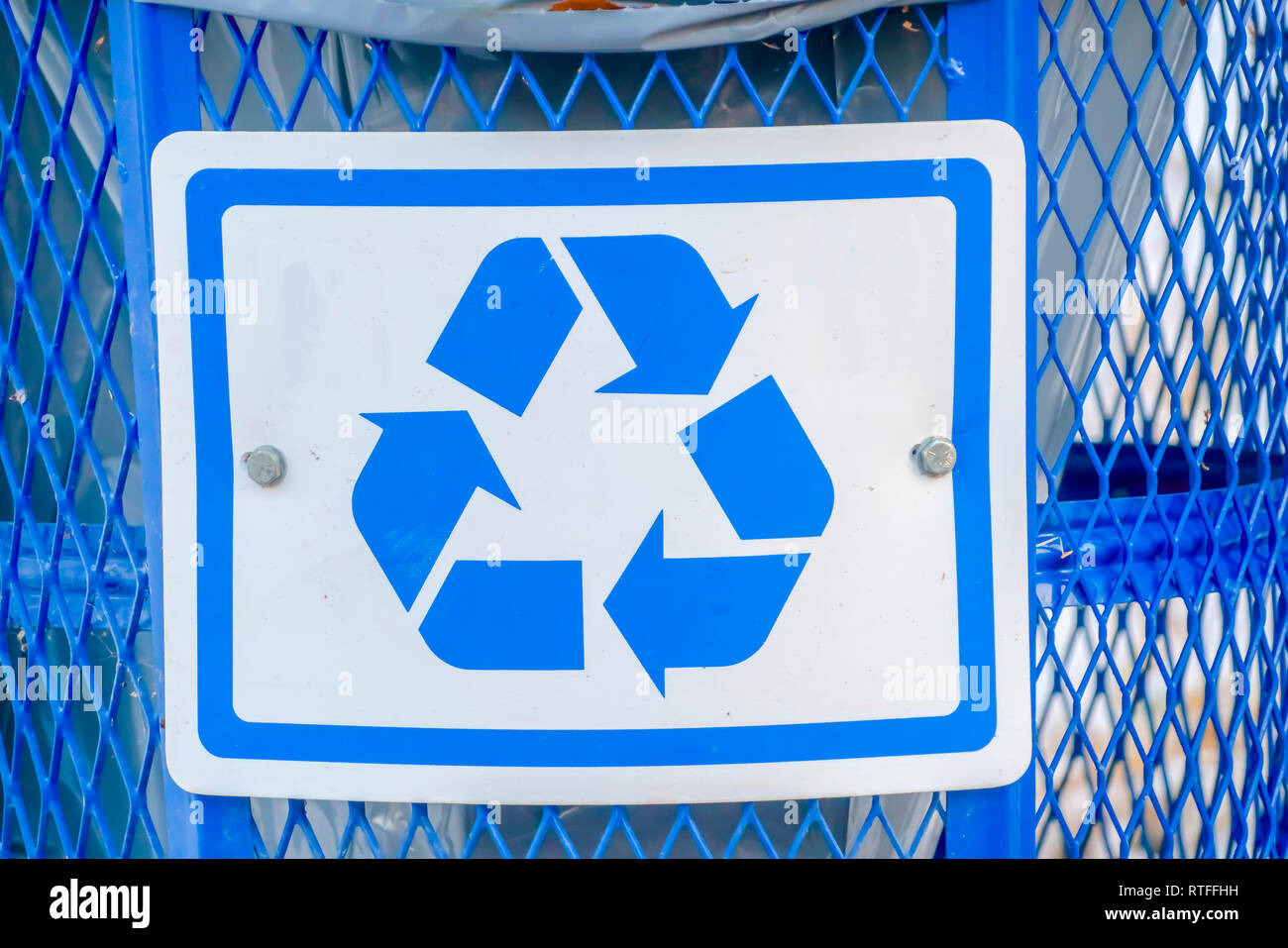 Contenedor de basura azul con un símbolo de reciclado. Vista de cerca de un  cesto de basura azul metálico con una bolsa de plástico interior. Un  símbolo de reciclado pueden verse en