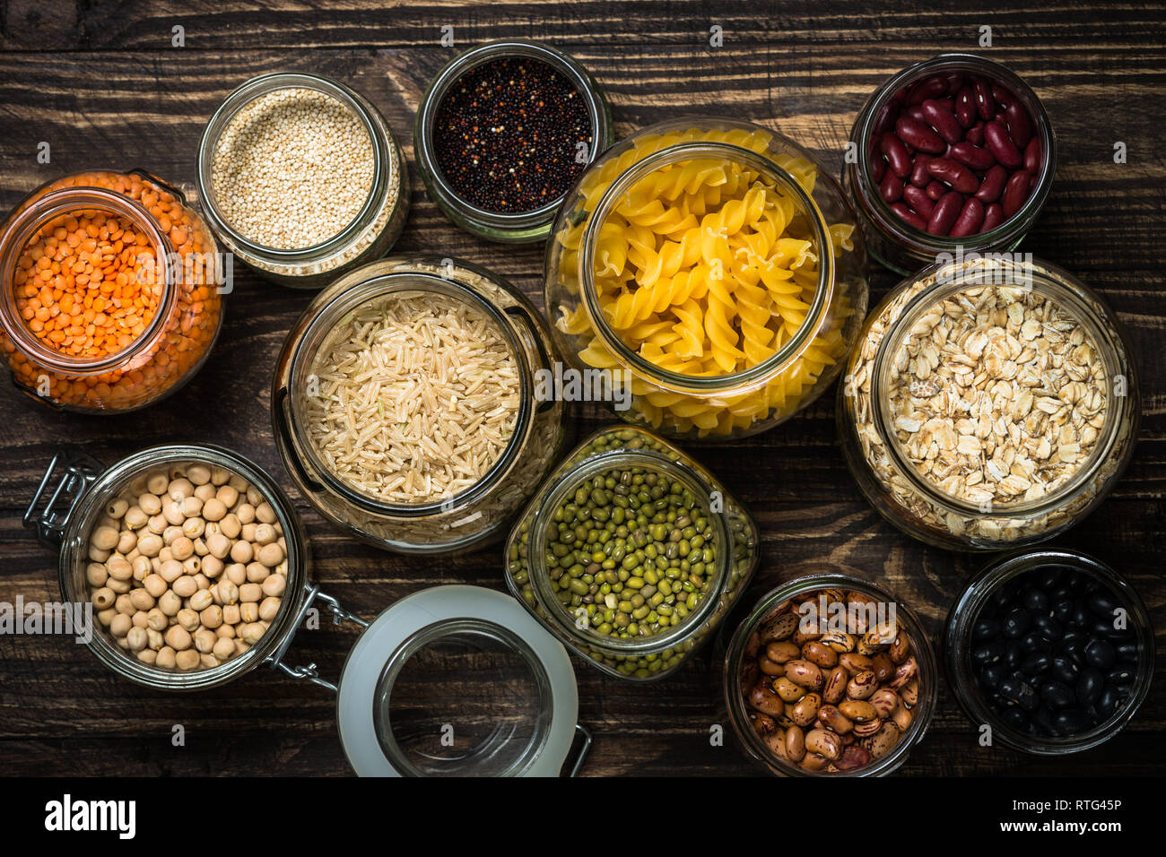 Los cereales, las legumbres y frijoles en tarros de vidrio sobre la mesa de madera oscura. Foto de stock