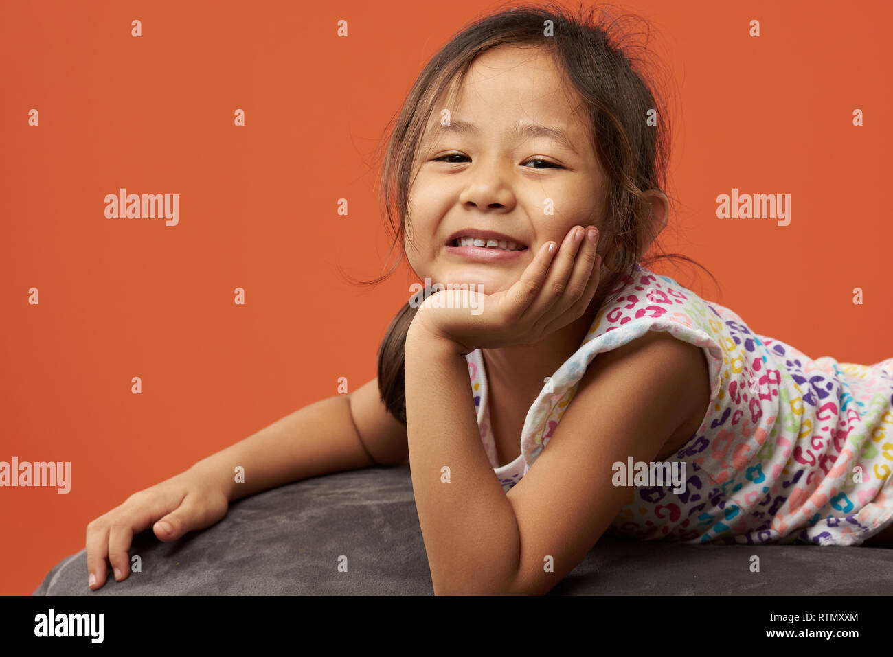 Retrato de muchacha asiática con la mano en el mentón aislado en color naranja Foto de stock