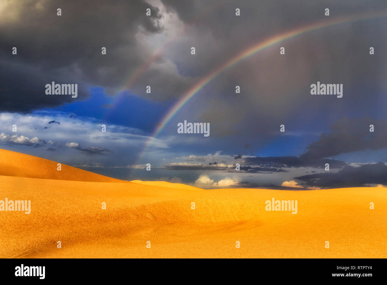 Tormenta de lluvia y arco iris sobre las dunas de arena del desierto en Stockton Beach en Australia - moody paisaje del parque nacional. Foto de stock