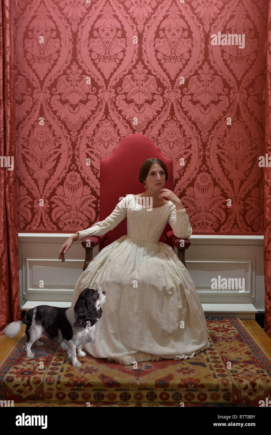 La reina Victoria sentada en un trono en Kensington Palace- la habitación  es rojo y ella lleva un vestido blanco. Su rey Charles Spaniel llamado dash  a sus pies Fotografía de stock -