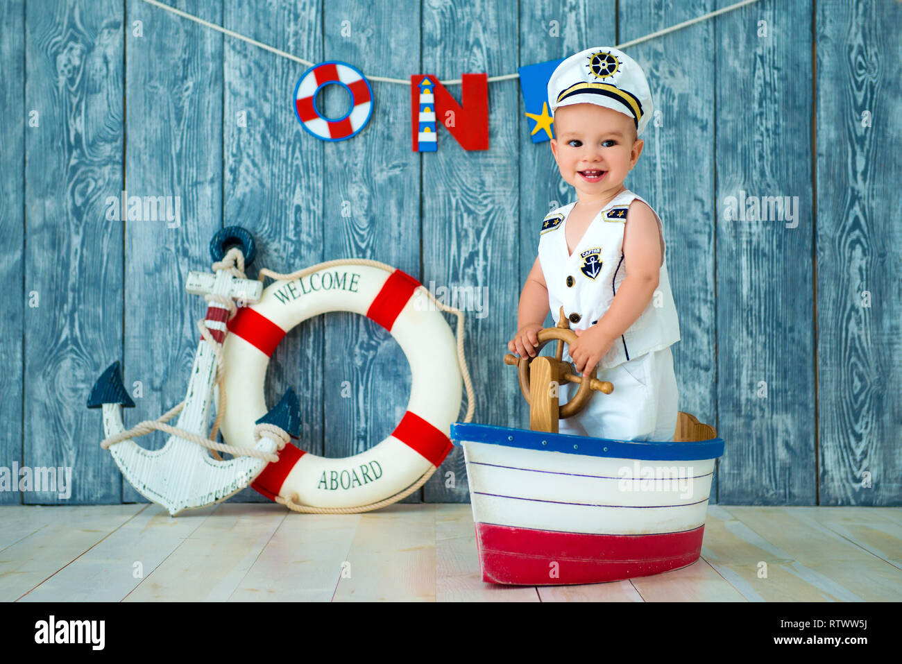 Sesión de fotos para un niño de un año. Mar pequeño capitán, marinero en el  barco de juguete con el volante de la dirección. Mar ancla y salvavidas en  gris de fondo