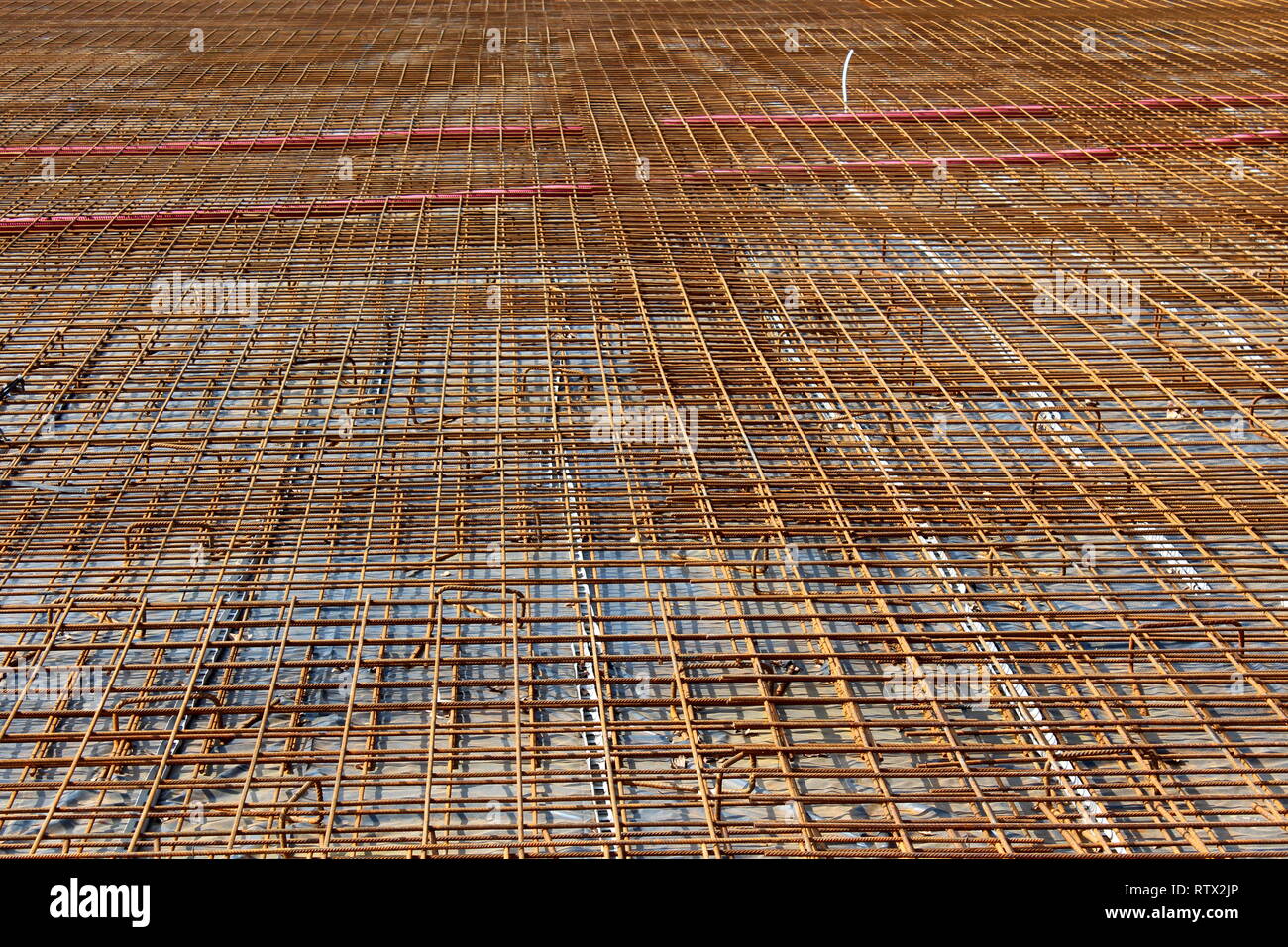 Densamente sentó Rusted metal construcción net encima de fuertes cimientos de hormigón en la construcción local sitio en días soleados Foto de stock