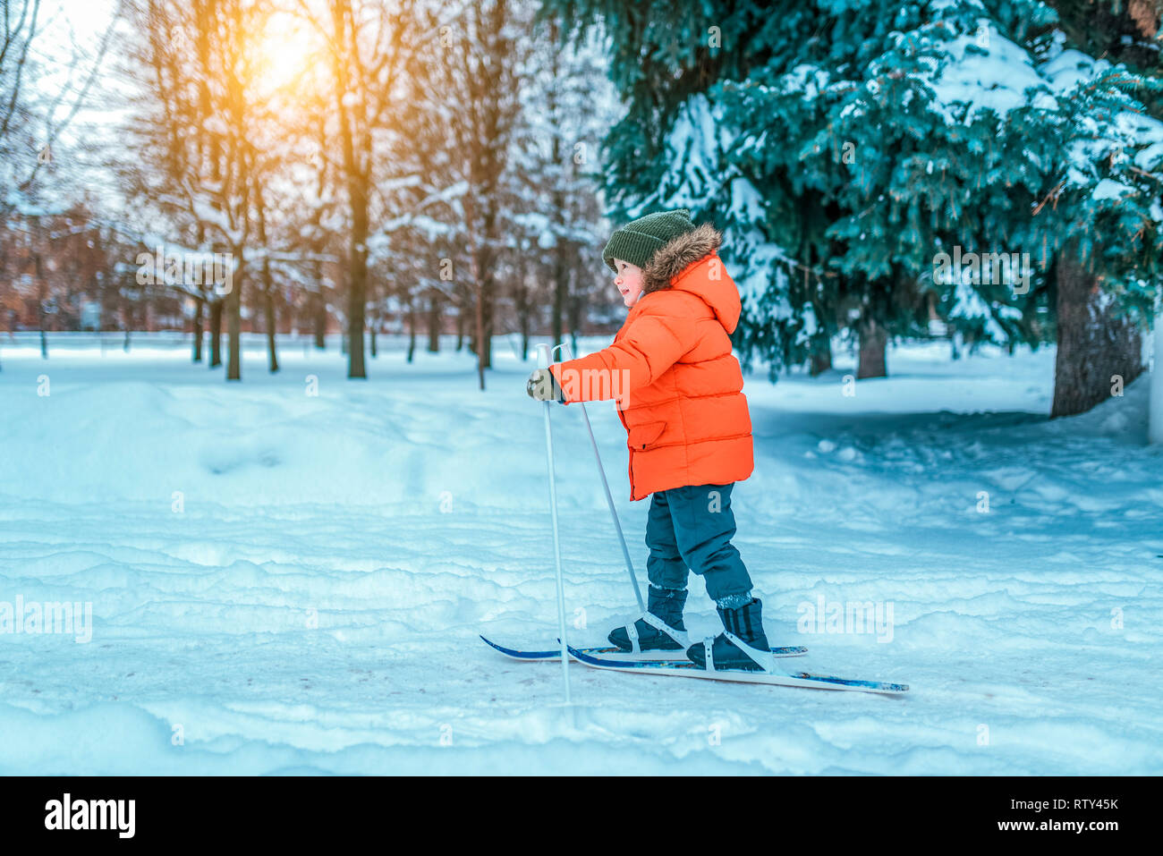 Un niño de 4-6 años en una chaqueta roja sobre esquís para niños. En invierno, en el parque de la ciudad, primeros pasos sobre los esquís, el comienzo de las actividades deportivas Foto de stock
