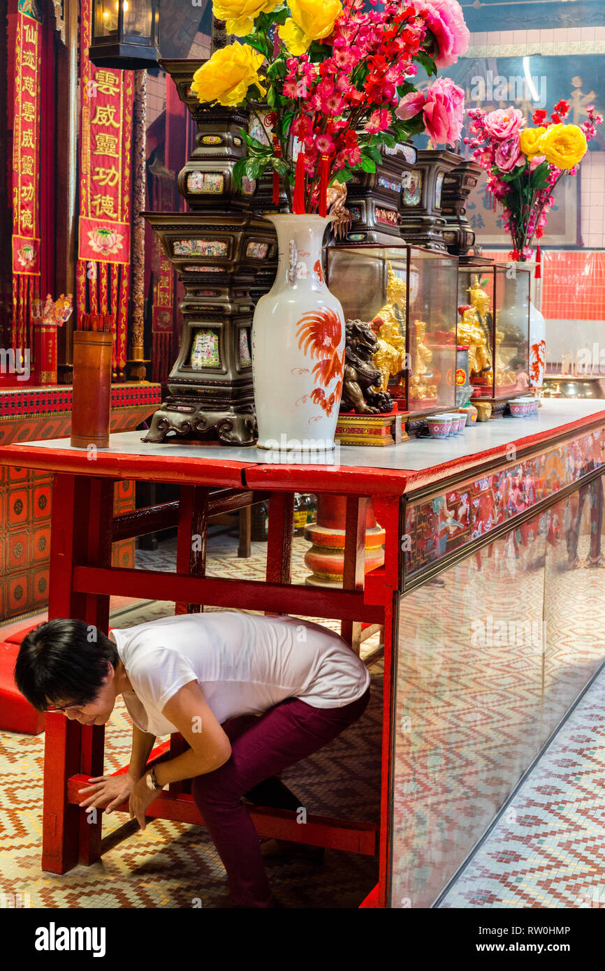 Adoradora reptando bajo la mesa delante del altar para ganar méritos y bendición, pecado Sze Si ya Templo Taoísta, Chinatown, Kuala Lumpur, Malasia. Foto de stock