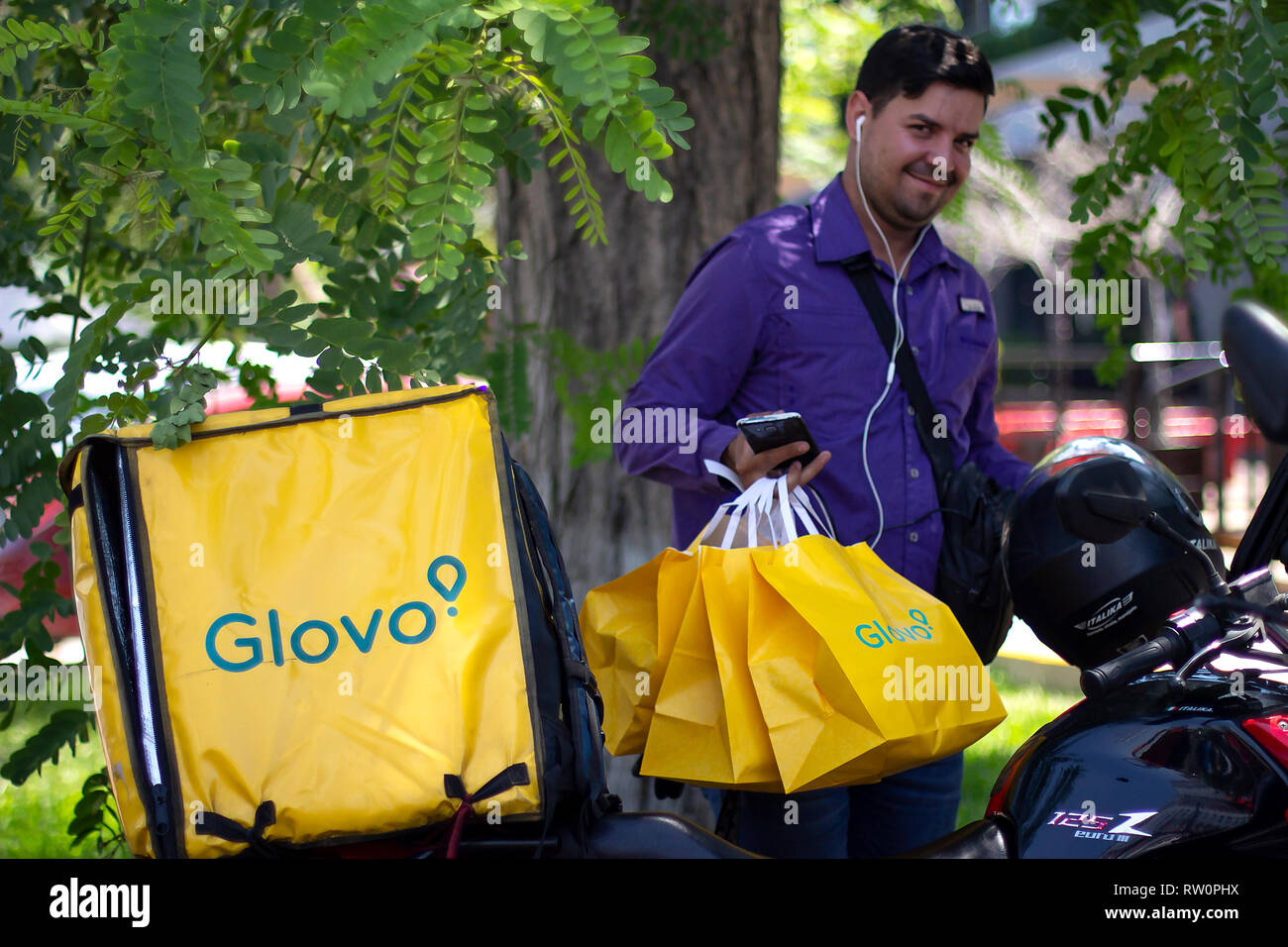 Lima, Perú - El 3 de marzo de 2019: El Hombre sonriendo con bolsas Glovo trabajando en el servicio de entrega de alimentos, de pie junto a su moto. Compartir economía colaborativa Foto de stock