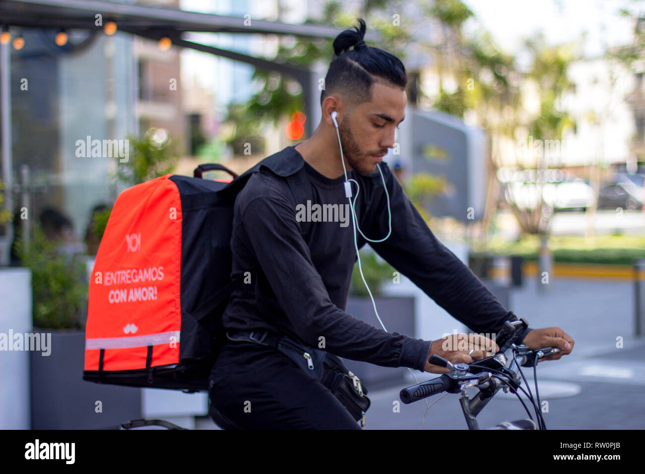 Lima, Perú - El 3 de marzo de 2019: buen mozo montando bicicleta Rappi trabajando para el servicio de entrega de alimentos, el control de la aplicación en su smartphone. Compartir colaboración Foto de stock