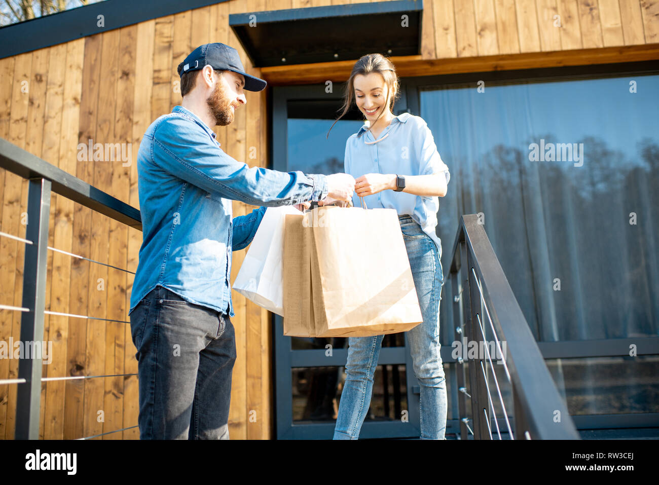 Hombre de entrega trayendo algunos bienes envasados en bolsas de papel para  una joven cliente a casa. Comprar ropa online y concepto de entrega  Fotografía de stock - Alamy