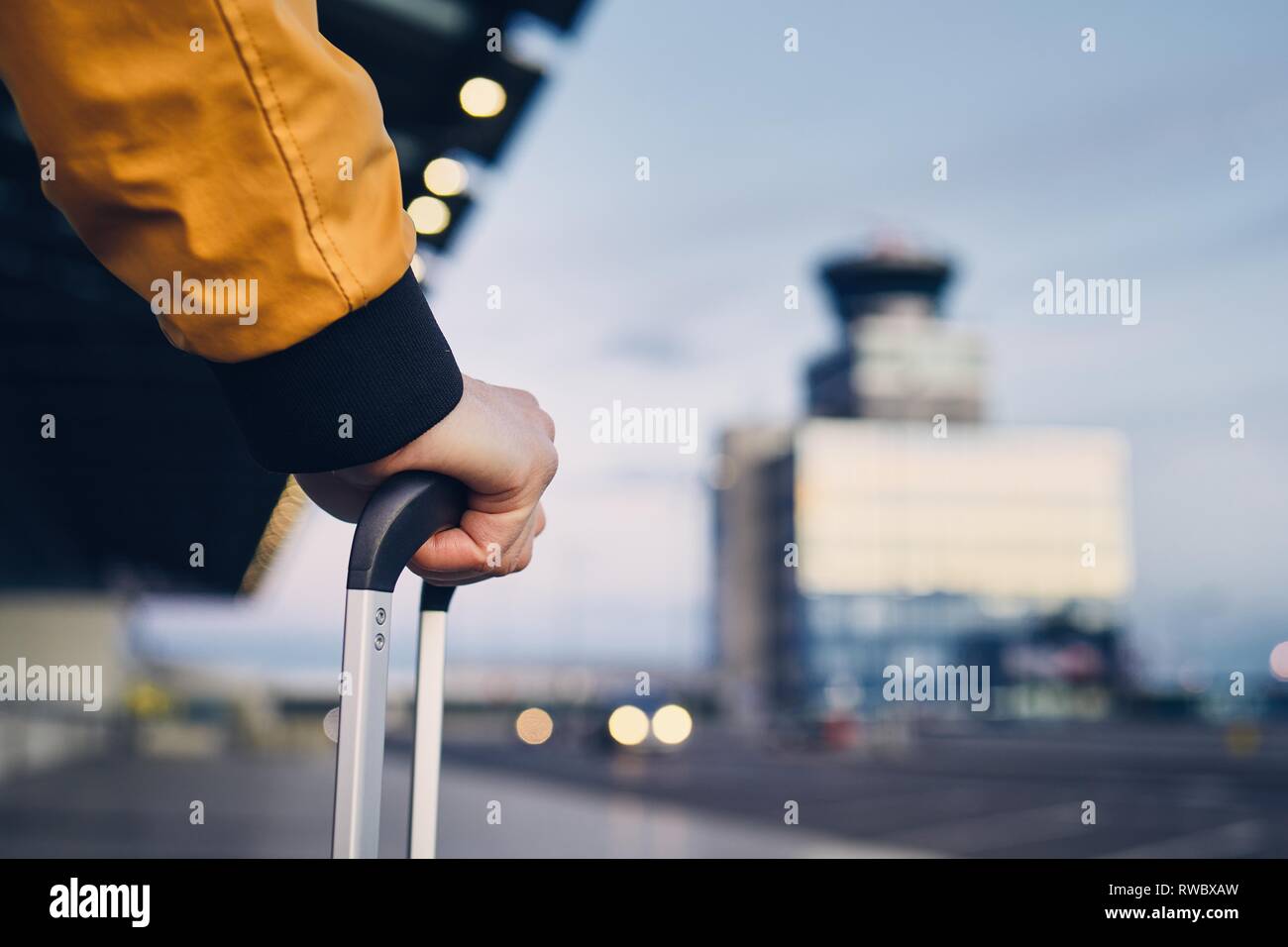 Mano del joven hombre sujetando el equipaje contra la terminal del aeropuerto. Foto de stock