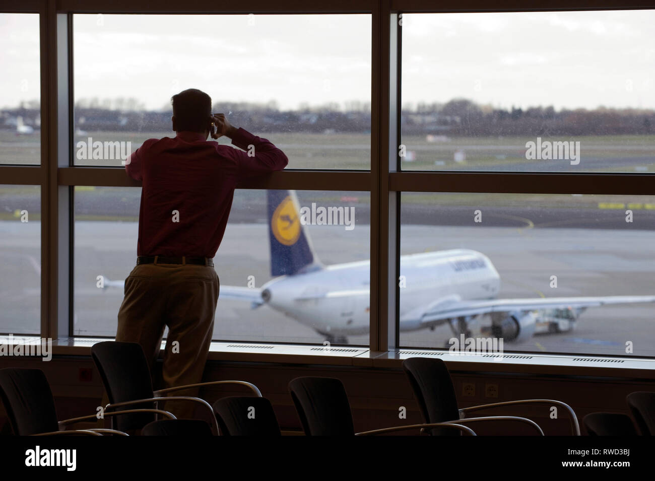 Ein Mann steht en einer Vortragspause am Fenster des Duesseldorfer Flughafen und eine Lufthansa Maschine schaut auf die auf dem Vorfeld parkt. [(C) Di Foto de stock