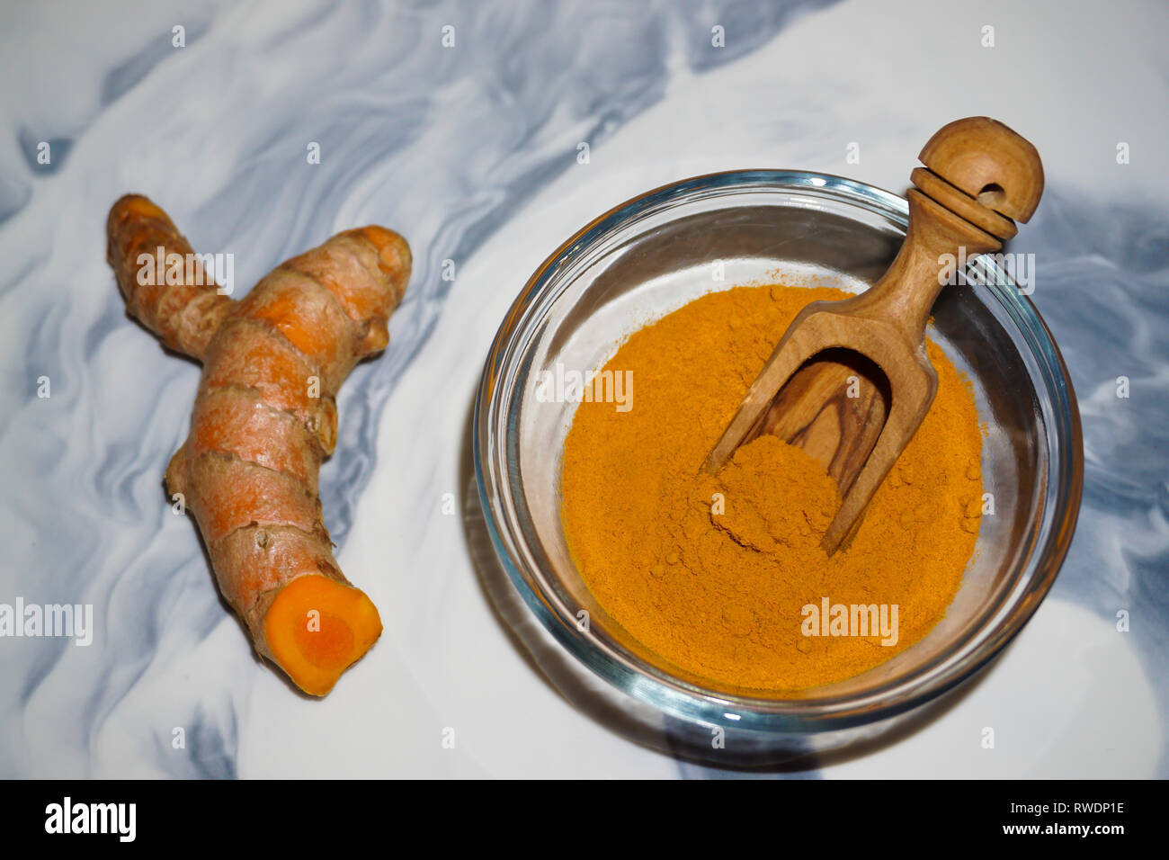 La cúrcuma en polvo en una cuchara de madera y el tazón de vidrio y fresco de raíz de cúrcuma. Foto de stock