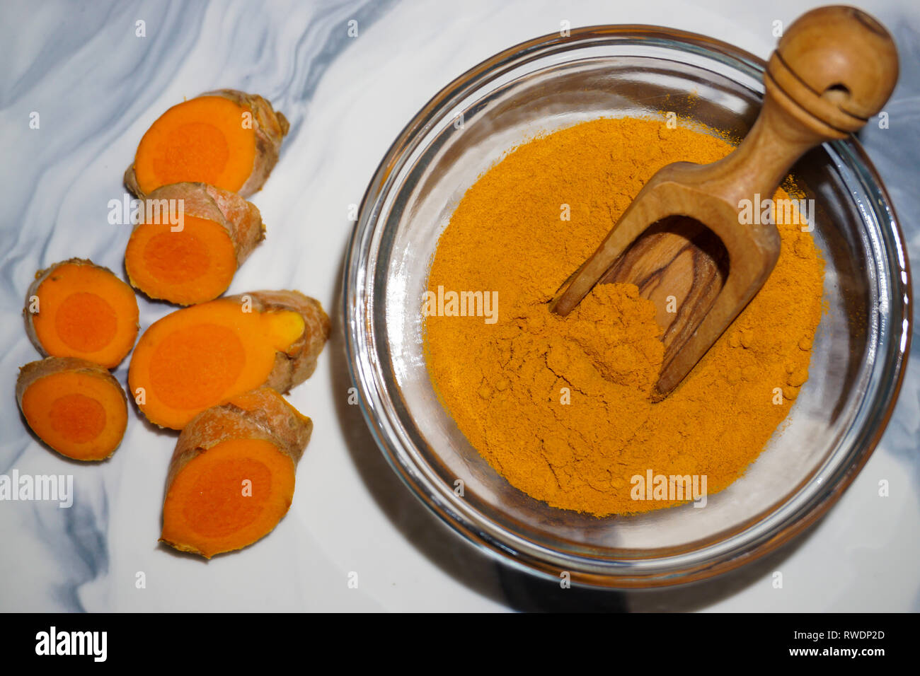 La cúrcuma en polvo en una cuchara de madera y el tazón de vidrio y fresco de raíz de cúrcuma. Foto de stock