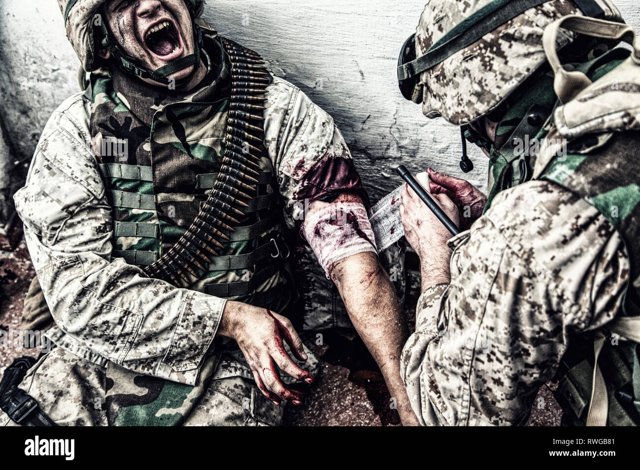Marine sufrimiento en dolor mientras un médico militar se aplica un vendaje para heridas de bala. Foto de stock