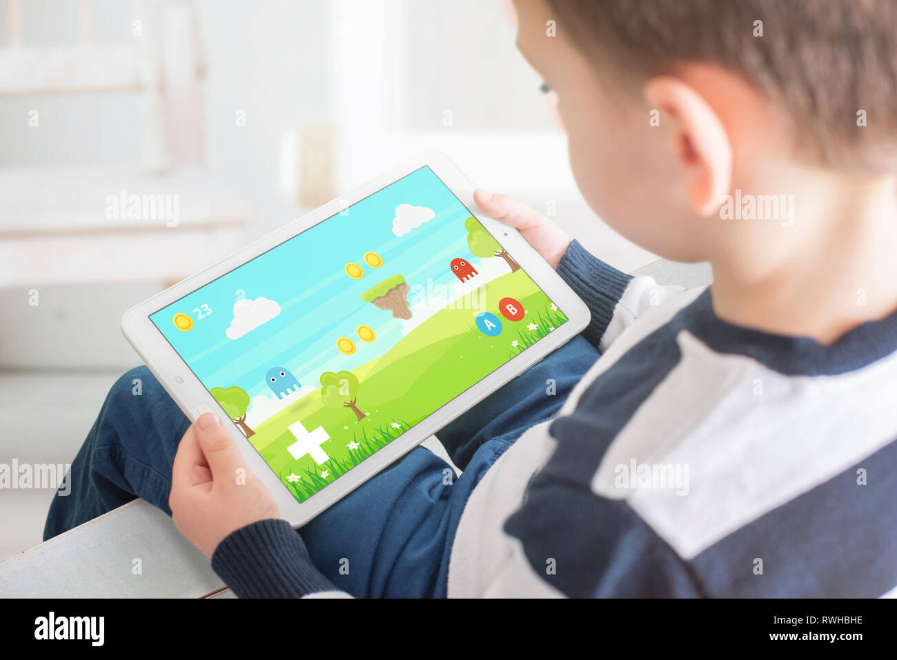Niño jugando en tableta blanca. En bacgkround interior. Juegos para chicos en dispositivos móviles concepto. Foto de stock