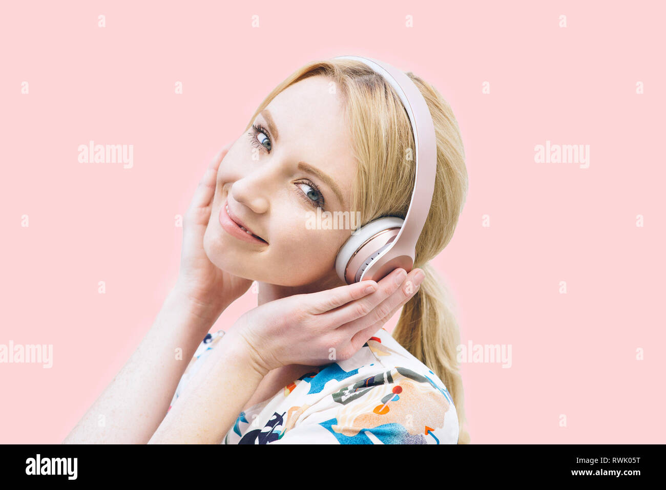 Vista frontal de una joven muchacha caucásica con auriculares y escucha música en un fondo de color rosa Foto de stock
