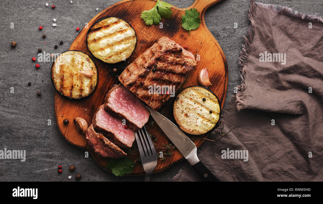 Filete de ternera bistec medio raro con hortalizas y especias sobre una tabla para cortar en rodajas. Vista desde arriba Foto de stock