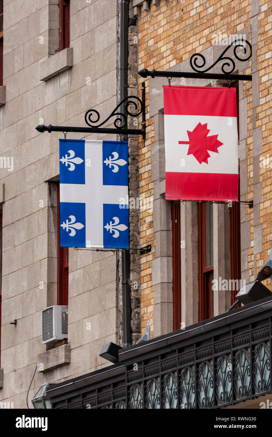 Bandera nacional canadiense y bandera provincial de Quebec colgando de los soportes de la señal de la vendimia en un edificio de ladrillo en Quebec, Canadá Foto de stock