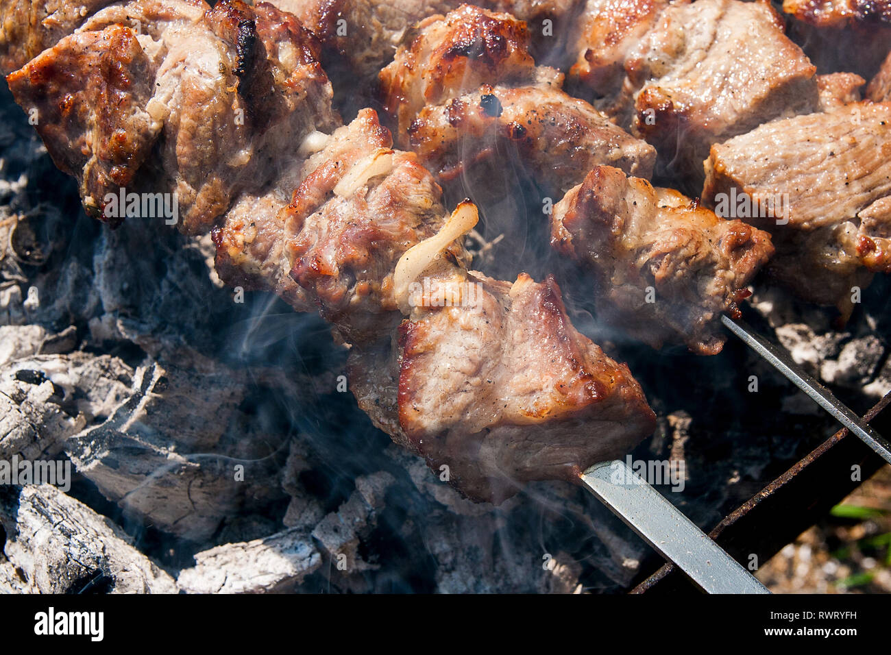 Parrilla de cocción de kebab en pincho de metal. Hecha pinchito de cubos de carne en las brochetas durante la cocción en el mangal en carbón al aire libre. Parrilla Foto de stock