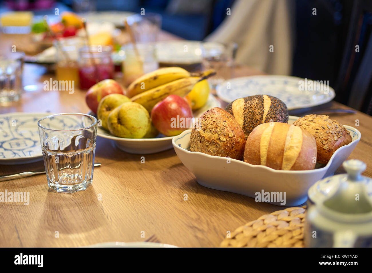 Mesa de madera para desayuno con frutas, verduras, atasco en frente de una cocina, se centran en rollos en primer plano Foto de stock