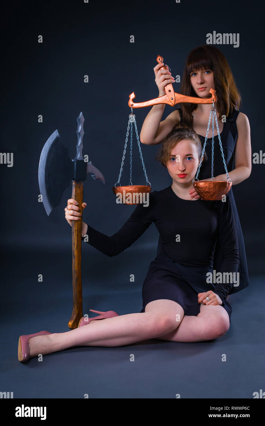 Dos niñas como guardianes de la ley, la justicia y los derechos humanos, sosteniendo en sus manos las escamas y la ax como instrumento de represalia Foto de stock