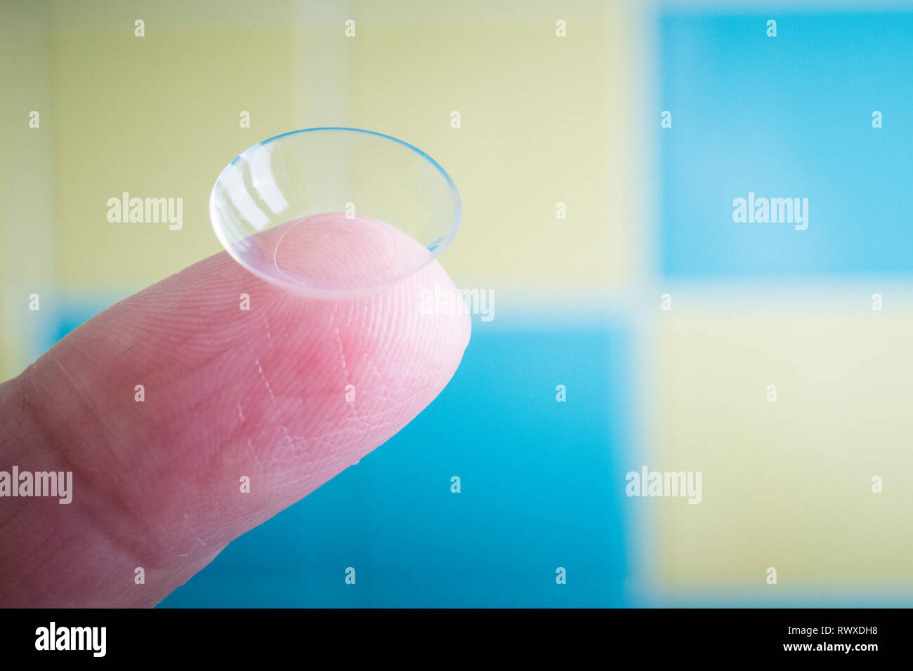 Lentes de contacto blandos en la punta del dedo, macro con fondo amarillo y  azul y luz natural Fotografía de stock - Alamy