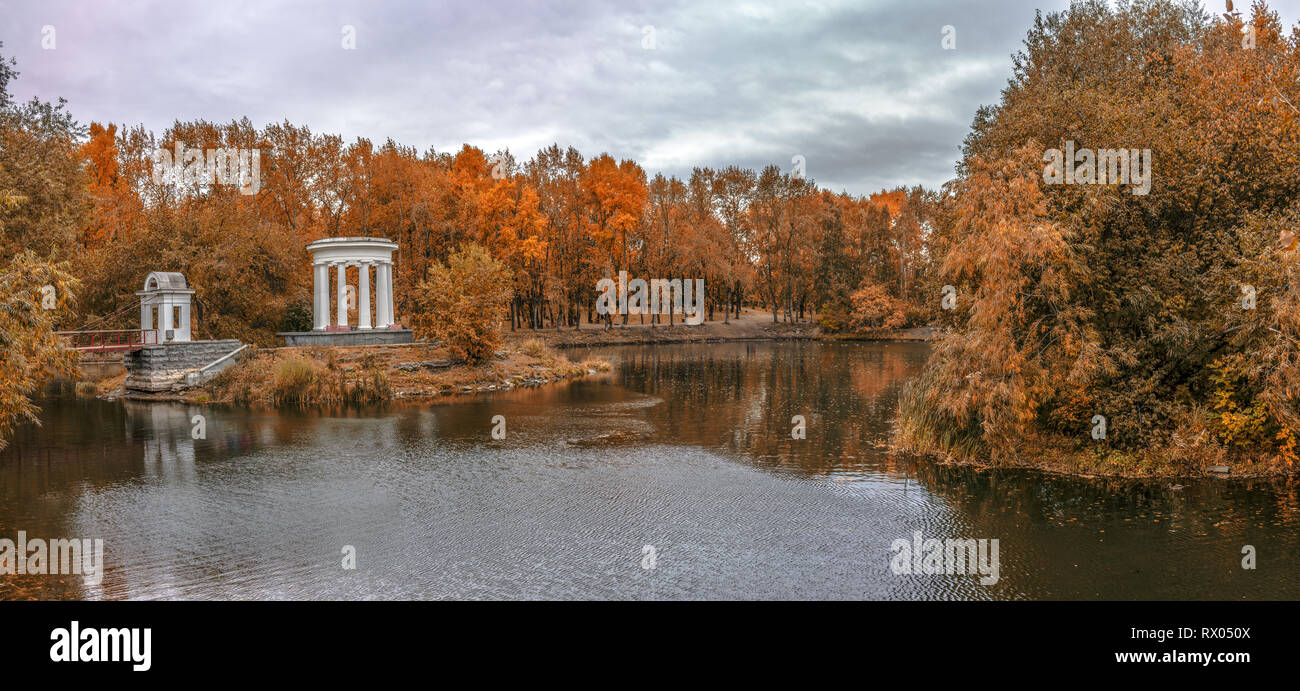 Estanque en un parque verde de la ciudad con una rotonda a finales del otoño dorado Foto de stock