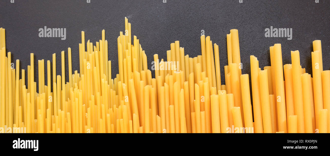 Comida italiana. Sin cocer los espaguetis y macarrones pasta seca sobre fondo negro, banner Foto de stock