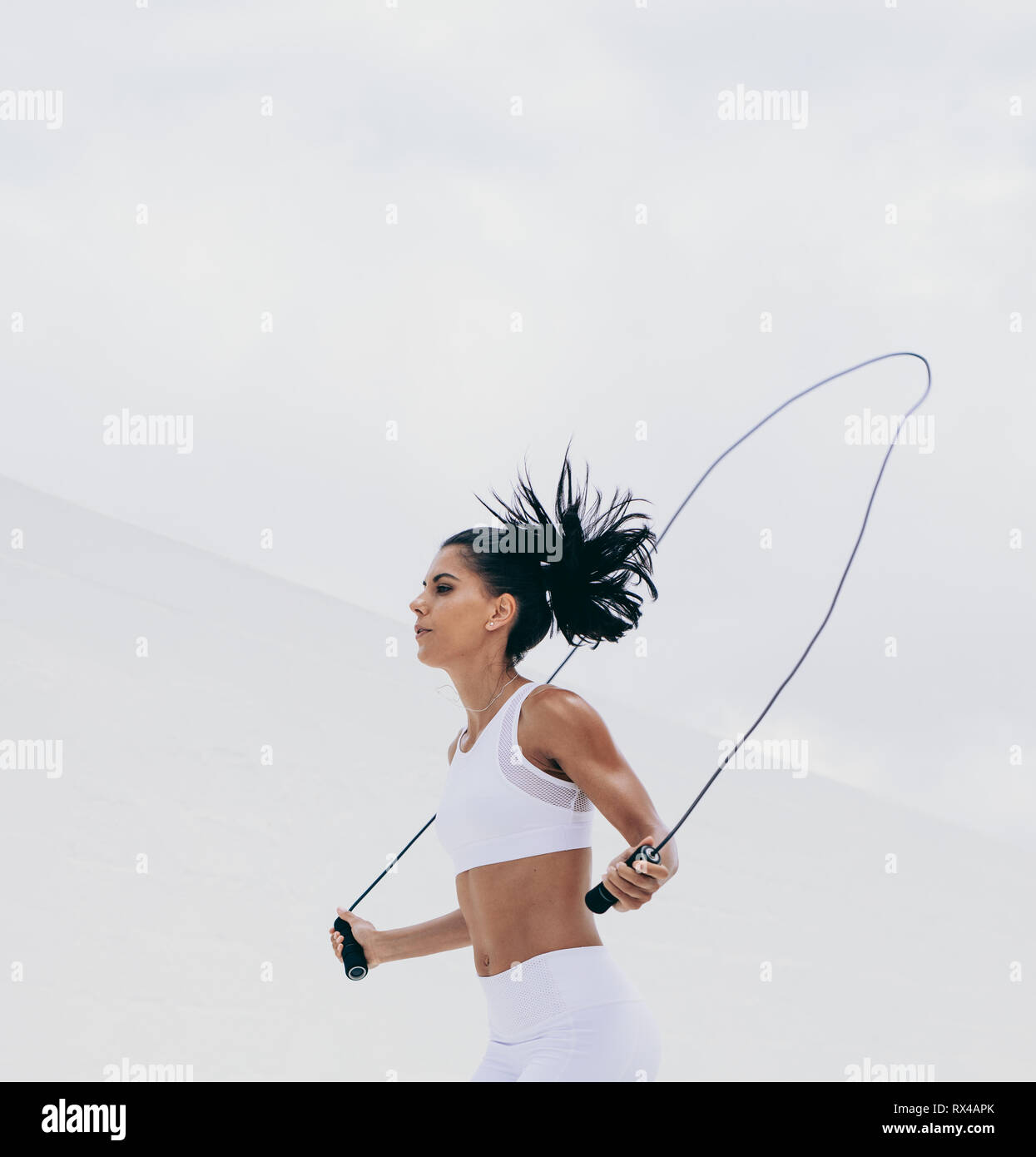 Recorta la foto de un atleta femenina en fitness wear trabaja con una cuerda. Vista lateral de una mujer realizando ejercicios de entrenamiento. Foto de stock