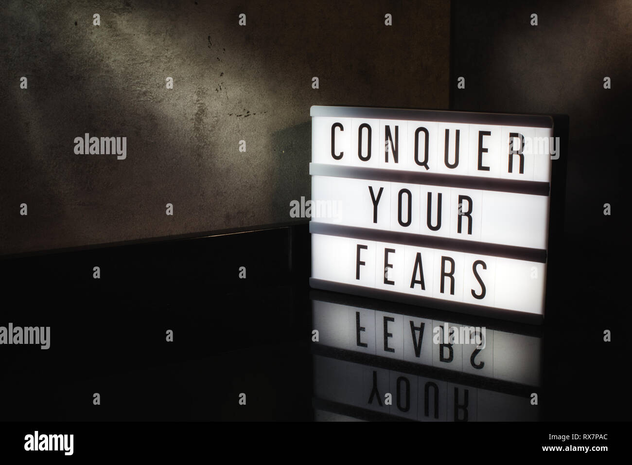 Conquistar tus temores mensaje de motivación en una caja de luz en un fondo moody cinematográfica Foto de stock