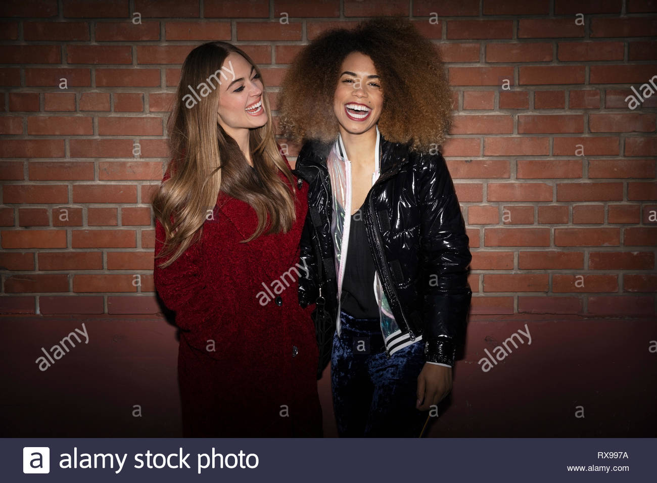 Retrato riendo mujeres jóvenes amigos que estaban de pie en la pared de ladrillo Foto de stock