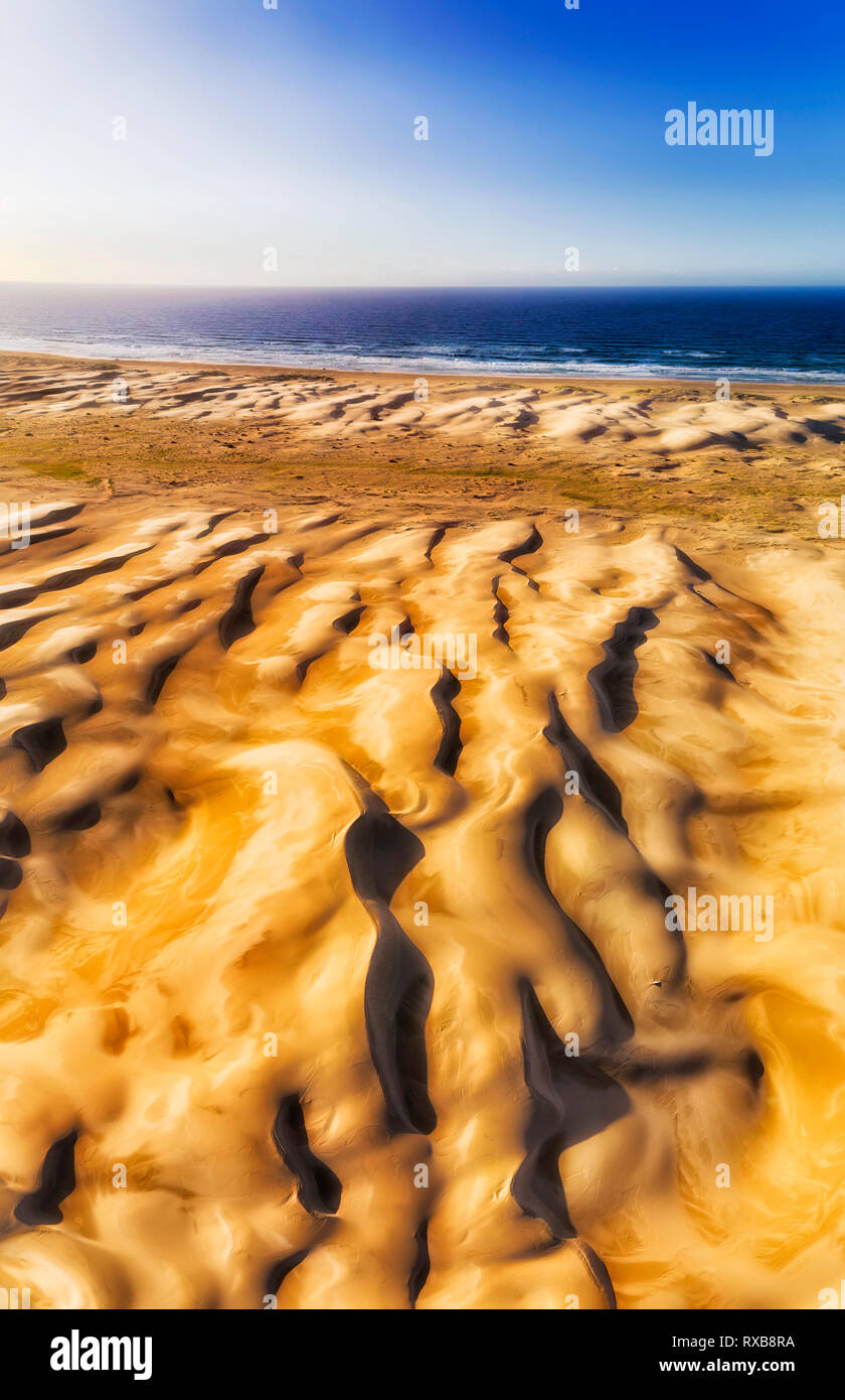 Y pulida superficie formada de dunas de arena en Stockton Beach frente al océano pacifico con fuertes vientos en antena panorama vertical de tierra a mar abierto un Foto de stock
