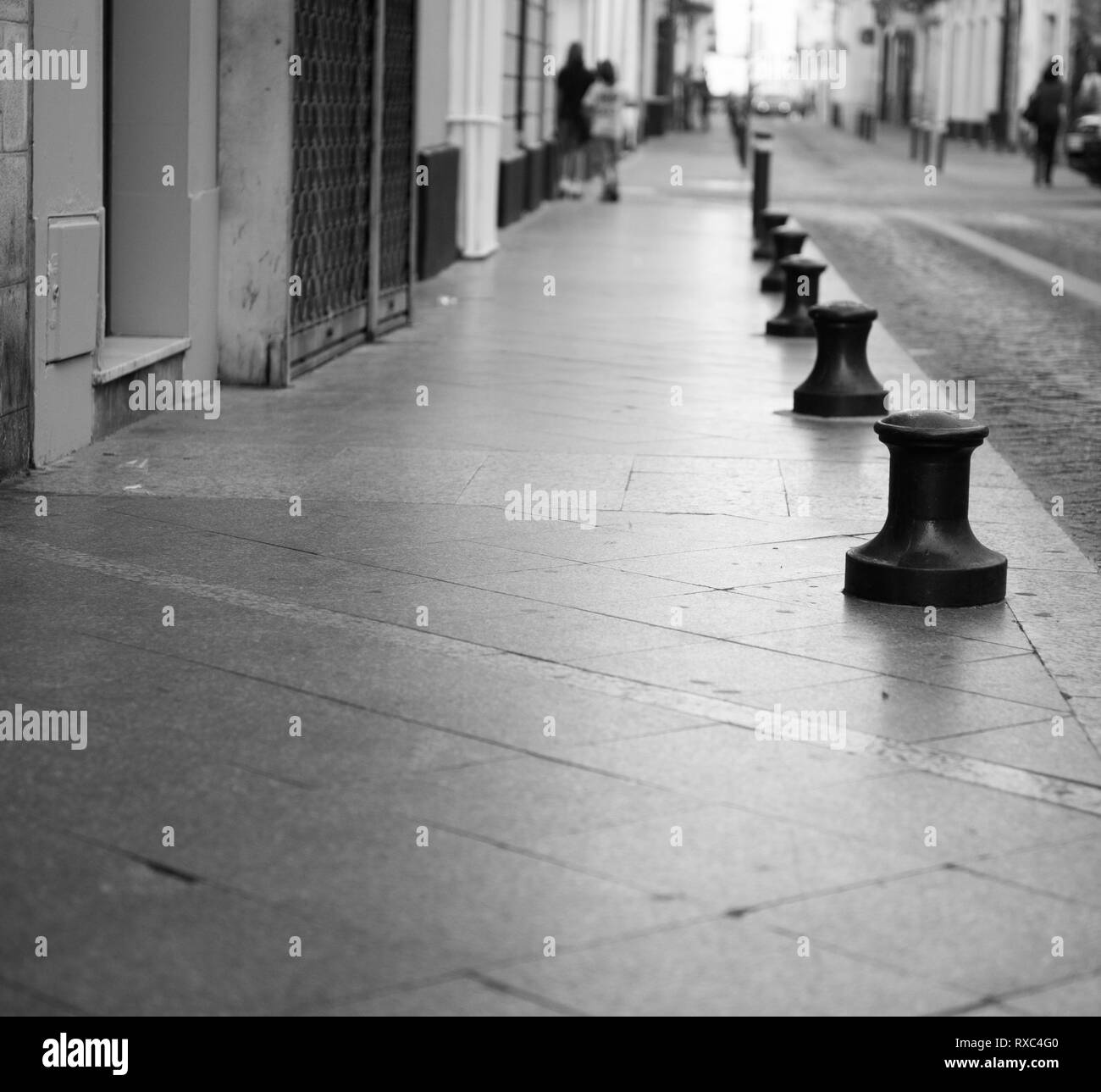 Línea de pilonas metálicas marcando el borde del pavimento en una calle vacía distantes inidentificables figura agregar una escala, mobiliario urbano bolardo Foto de stock