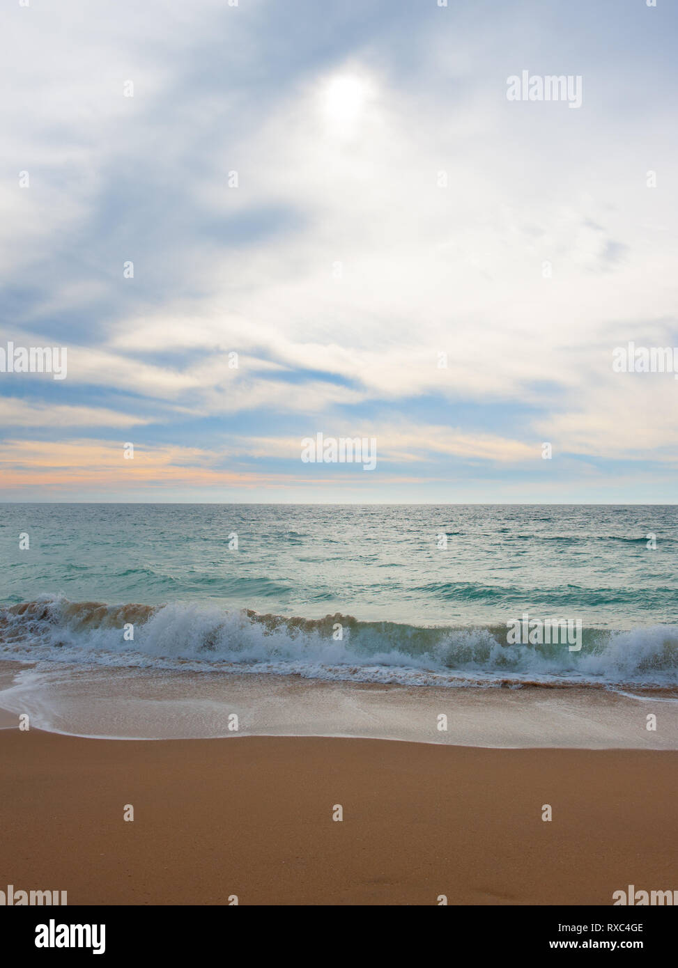 Seascape pacífica con las olas lamiendo suavemente a la orilla del mar en la arena. El sol se filtra a través de la luz acuosa nubes que cubren el cielo Foto de stock
