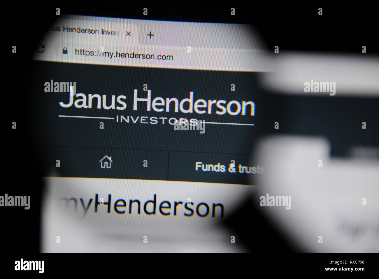 El Janus Henderson web es visto a través de una lupa. Janus Henderson se formó en 2017 cuando Janus Capital Group y Henderson Global Investor Foto de stock