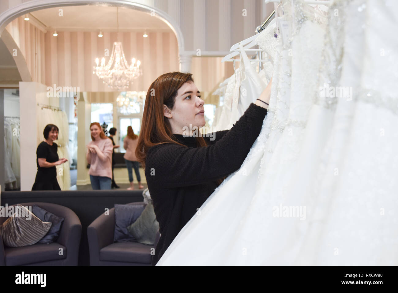 2 asistentes de fabricación están ayudando a una hermosa niña de cabello  rojo en una tienda de vestidos de boda para elegir su vestido de ensueño  Fotografía de stock - Alamy