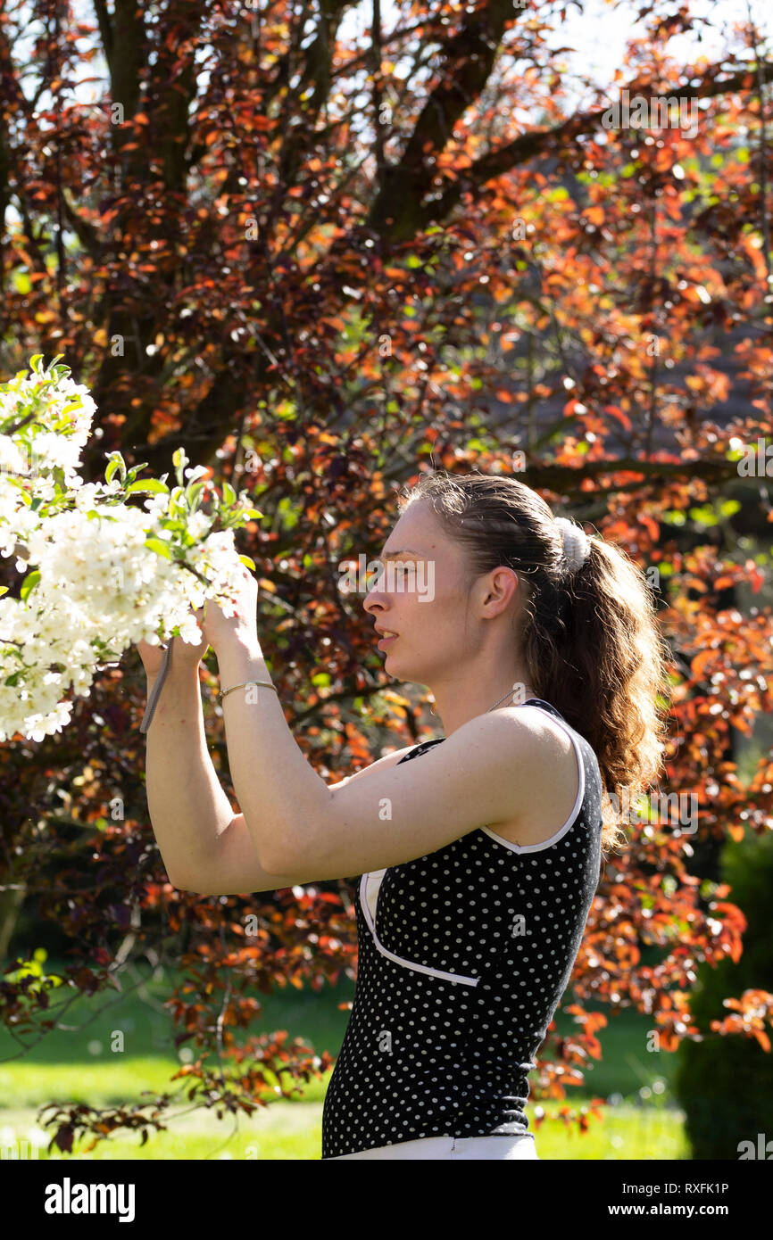 Joven mujer caucásica en un vestido sin mangas de puntos blancos toma una foto de Apple tree blossoms con una cámara compacta en un día soleado. Foto de stock