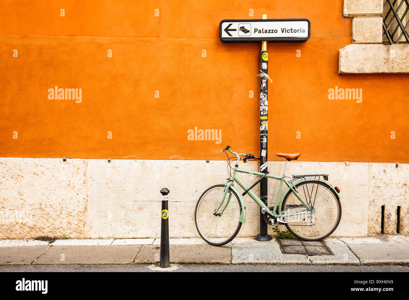 Una bici verde encadenado en una dirección Palazzo Victoria polo en un  callejón con una pared de color naranja. Verona, Italia Fotografía de stock  - Alamy