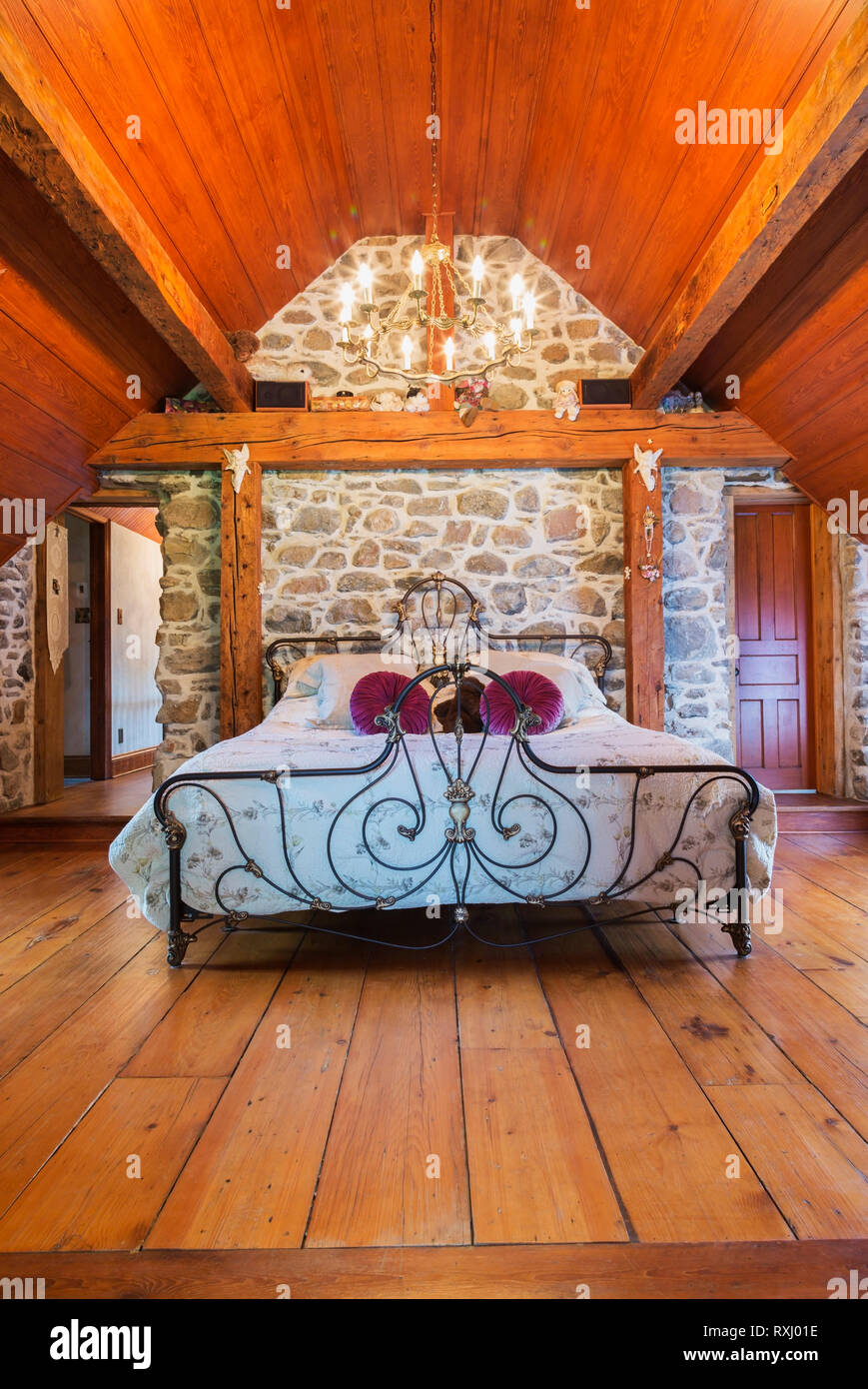Cama tamaño king con cabecero de hierro forjado antiguo y reposapiés en el  dormitorio principal con tablones de madera de pino en el piso de arriba  dentro de una antigua casa de
