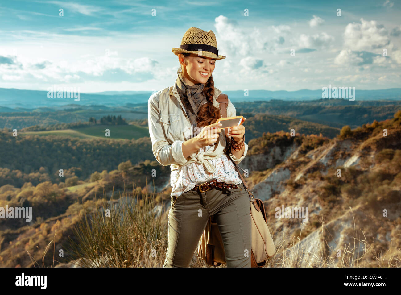 Turismo de Aventura sonriente mujer en ropa de senderismo con bolsa con  smartphone utilizando app contra el paisaje de verano de Toscana, Italia  Fotografía de stock - Alamy