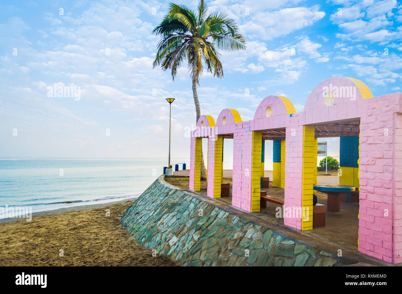 Lugar de descanso en la playa con ladrillos amarillos y rosados con mar calmo y un solitario árbol de coco en el fondo. De Muscat, Omán. Foto de stock