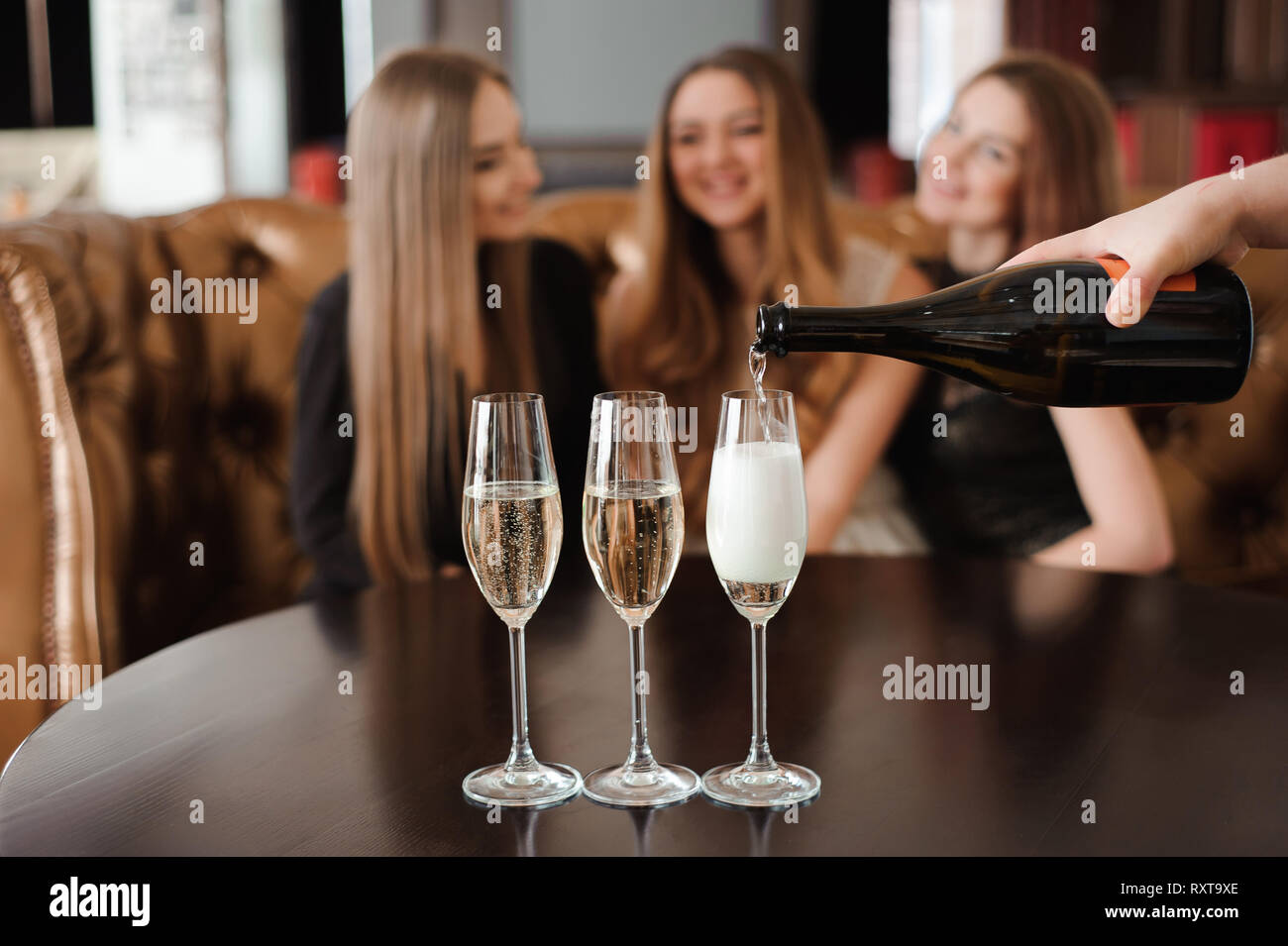 El hombre rellena copas de champán para tres hermosas mujeres jóvenes en el  restaurante Fotografía de stock - Alamy